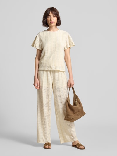 Kobiece modelka nosi bluzkę z krótkim rękawem z haftem angielskim model 'CASSANDRA' od Vero Moda, efekt: jednolity kolor, krój regular fit, okrągły dekolt, wykończenie materiału: haft angielski, całkowity widok z przodu.