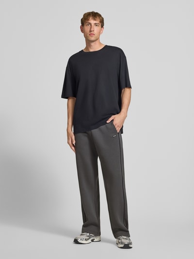 Männermodel trägt Straight Fit Sweatpants aus reiner Baumwolle mit Label-Patch von REVIEW, dunkelgrau, elastischer Bund, Eingrifftaschen, Ganzkörperansicht von vorne.