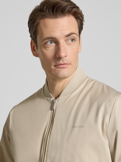 Männermodel trägt Bomberjacke mit Reißverschlusstaschen Modell 'MATTE' von Calvin Klein in Beige mit kurzem Stehkragen, Nahaufnahme Oberkörper.