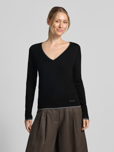 Frauenmodel trägt Slim Fit Longsleeve aus reine Viskose Modell 'Maglia Chiusa' von Liu Jo White, V-Ausschnitt, Logo-Detail, schwarze Farbe, Ganzkörperansicht von vorne.