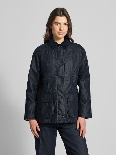 Modelka kobieca nosi Wachsjacke aus reiner Baumwolle od Barbour w kolorze granatowym, krój regular fit, wodoodporna, z patką na kieszeniach; widok całej sylwetki z przodu.