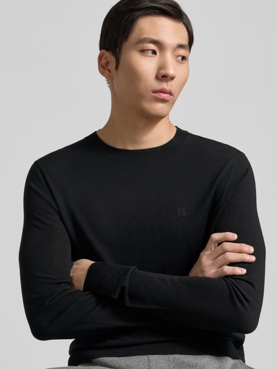 Männermodel trägt Wollpullover aus reiner Wolle von Dsquared2, fein gestrickt, schwarz, Rundhalsausschnitt, Nahaufnahme Oberkörper.