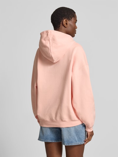 Frauenmodel trägt Oversized Hoodie mit Logo-Detail von Anine Bing aus Reine Baumwolle in zartem Rosa, Känguru-Tasche, Oversized-Fit, elastische Abschlüsse, Rückenlänge bei Größe S: 64 cm, Ganzkörperansicht Rückansicht.