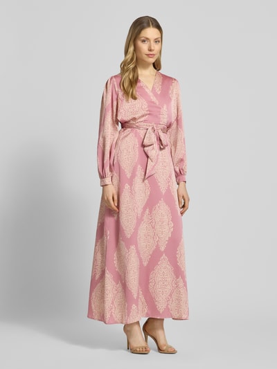 Frauenmodel trägt Regular Fit sukienka wieczorowa z satyny model 'Bretti' od Neo Noir z wzorem paisley na całej powierzchni, długi rękaw, dekolt w serek, taliowany krój, odpinana materiałowa tasiemka, kopertowy styl, zakończenia rękawów, długość tyłu w rozmiarze 36: 131 cm, szerokość w rozmiarze 36: 48 cm, długość rękawów w rozmiarze 36: 63 cm, różowe i kremowe odcienie, delikatna tekstura, wzór na całej powierzchni. Ganzkörperansicht von vorne.