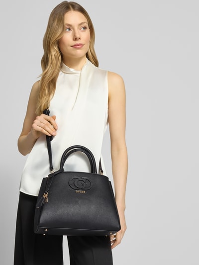 Kobiece model prezentuje Handtasche in Leder-Optik Modell 'Isola' od Guess, czarny kolor, faktura skóry, widok z przodu, zbliżenie na górną część ciała. Szerokość w rozmiarze 1: 31 cm, długość 22 cm, głębokość 14 cm, długość paska na ramię 123 cm, podzielona komora główna na zamek, pasek na ramię i odpinana rączka, detal z logo.