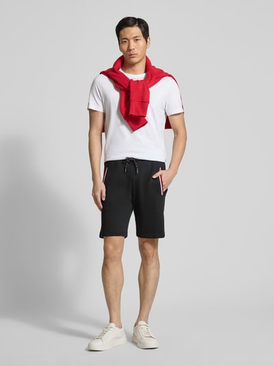 Męski model nosi Shorts mit elastischem Bund od Christian Berg Men, czarny kolor, krój regular fit, kieszenie z kontrastowymi paskami, bawełna z elastanem, szerokość w rozmiarze M: 43 cm, długość nogawki od wewnątrz w rozmiarze M: 23 cm, widok całej sylwetki z przodu.