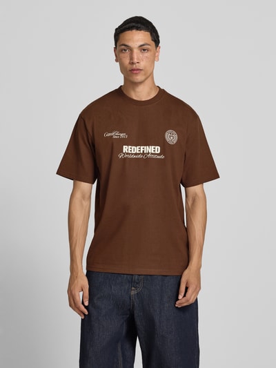 Männermodel trägt braunes Herren T-Shirt mit Statement-Print und Rundhalsausschnitt von Redefined Rebel, Baumwoll-Mix, Relaxed-Fit, Modell 'Bruno', Rückenlänge bei Größe M: 70 cm, Ganzkörperansicht von vorne.