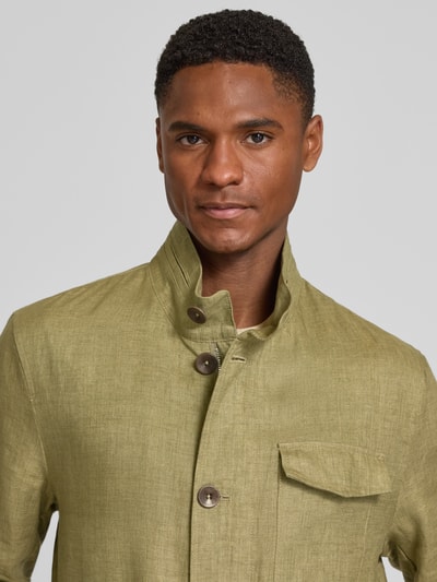 Männermodel trägt Leinenjacke mit Stehkragen und Pattentaschen von bugatti, len, krój regular fit, listwa guzikowa, kieszenie z patką, kolor oliwkowy, Nahaufnahme Oberkörper. Długość tyłu w rozmiarze 50: 74 cm, szerokość ramion w rozmiarze 50: 46 cm, szerokość klatki piersiowej w rozmiarze 50: 55 cm, długość rękawów w rozmiarze 50: 64 cm.
