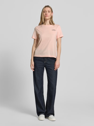 Modelka kobieca nosi damski t-shirt z nadrukiem z logo i okrągłym dekoltem od Gant, bawełna, krój regular fit, długość tyłu w rozmiarze S: 57 cm, widok całej sylwetki z przodu.
