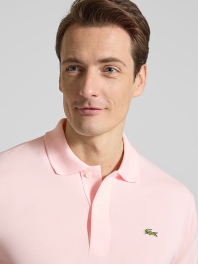 Mężczyznamodel nosi Regular Fit Poloshirt aus reiner Baumwolle od Lacoste, efekt: jednolity kolor, wyhaftowane logo, kołnierzyk polo, krój regular fit, krótki rękaw, zakończenie: prążkowane, z bocznymi rozcięciami, wykończenie materiału: pika, materiał: bawełna, zbliżenie na górną część ciała.