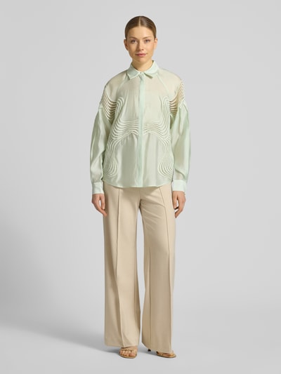Vrouwenmodel draagt Regular Fit blouse met overhemdkraag, model 'MOLLY' van Copenhagen Muse, verborgen knoopsluiting, ruglengte maat S 67 cm, mouwlengte maat S 76 cm, lichtgroen met golvende textuur, rechte vormen, beige broek, volledig frontaal zicht.