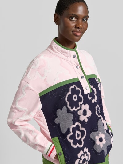Frauenmodel trägt Relaxed Fit Pullover aus Viskose-Mix mit Troyer-Kragen von Marc Cain, florales Design in Rosa, Dunkelblau und Grün, Nahaufnahme Oberkörper. Damen Pullover, Rückenlänge 62 cm, Ärmellänge 54 cm.