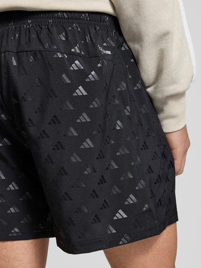 Männermodel trägt Regular Fit Sport-Shorts mit Allover-Muster von adidas Training, elastyczny pas, boczne kieszenie na zamek, wzór na całej powierzchni, krój regular fit, Ganzkörperansicht Rückansicht.