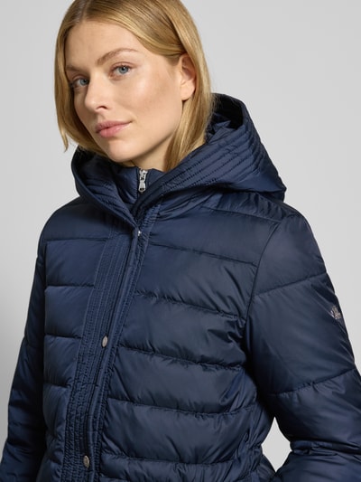 Vrouwenmodel draagt Daunenmantel mit Kapuze van Lauren Ralph Lauren, getailleerd, donkerblauw, met capuchon en steekzakken, close-up bovenlichaam.