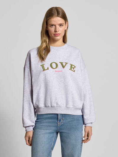 Frauenmodel trägt Sweatshirt mit Statement-Stitching und Rundhalsausschnitt von OH APRIL aus reiner Baumwolle im Regular-Fit, meliert, Ganzkörperansicht von vorne.