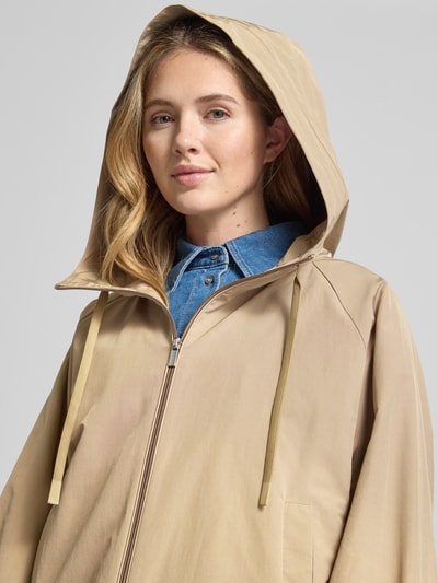 Frauenmodel trägt Relaxed Fit Regenjacke mit Baumwoll-Anteil Modell 'ROMANA' von Weekend Max Mara in Beige mit Kapuze und Logo-Patch, Nahaufnahme Oberkörper.