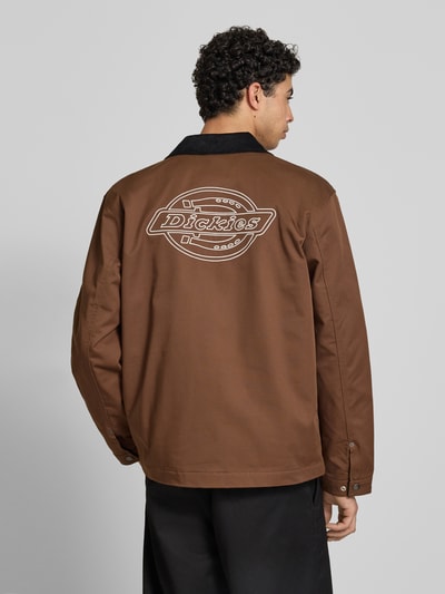 Männermodel trägt Jacke mit Umlegekragen und Label-Detail van Dickies in bruin met materiaalmix en katoenmix, regular fit, platte kraag, knoopsluiting, steekzakken, labeldetail, ruglengte maat M 75 cm, schouderbreedte 47 cm, borstwijdte 64 cm, mouwlengte 66 cm. Ganzkörperansicht Rückansicht.