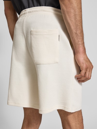 Männermodel trägt Shorts aus Baumwoll-Mix mit Strukturmuster Modell 'KNOX' von Redefined Rebel, Relaxed-Fit, Bund mit Tunnelzug, Strukturmuster, Einzel-Gesäßtasche, Farbe Beige, Ganzkörperansicht Rückansicht, Herren Shorts, Bundweite bei Größe M: 40 cm, Innenbeinlänge bei Größe M: 23 cm.
