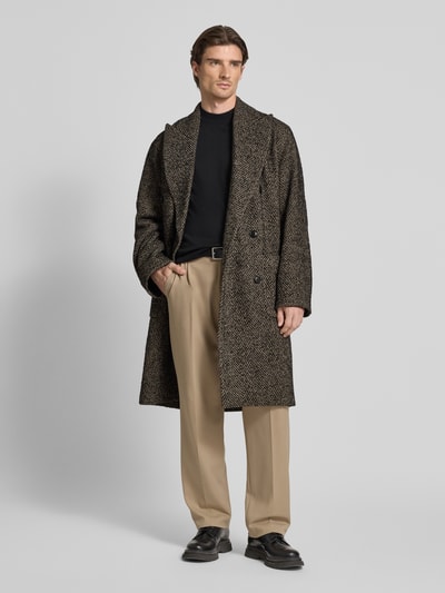Męskil model nosi Mantel aus Woll-Mix Modell 'MATESSO' od Drykorn, melanż szaro-czarny, krój relaxed fit, długość do kolan, dwurzędowy, klapy z wywinięciem, naszywane kieszenie, całkowita długość 113 cm w rozmiarze M, szerokość w rozmiarze M 44 cm ramiona, 53 cm klatka piersiowa, długość rękawa 69 cm, całkowity widok z przodu.