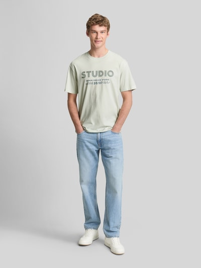 Männermodel trägt Relaxed Fit T-Shirt aus reiner Baumwolle von Tom Tailor Denim in Optik: Unifarben mit Label-Print, Ganzkörperansicht von vorne.