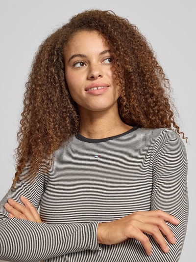 Vrouwenmodel draagt Slim Fit Langarmshirt aus Baumwoll-Mix van Tommy Jeans in fijngebreide katoenmix met gestreept allover-patroon, logo-stitching en ronde hals, close-up bovenlichaam.