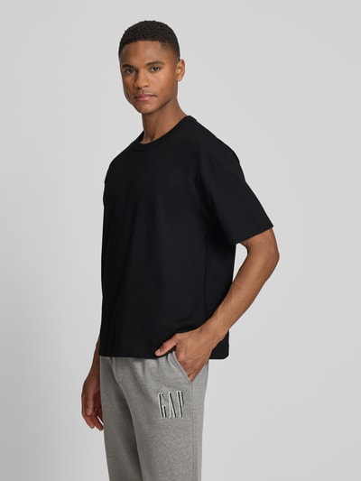 Männermodel trägt Cropped T-Shirt mit Rundhalsausschnitt von GAP in Schwarz, reine Baumwolle, glatte Textur, Ganzkörperansicht von vorne.