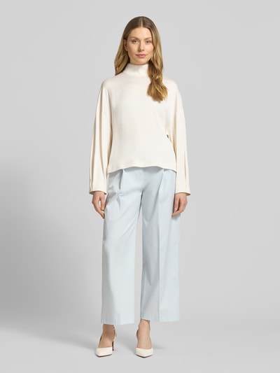 Kobiece modelka ma na sobie Relaxed Fit bluzka z stójką model 'ALVARA' od Drykorn, mieszanka materiałów z dodatkiem streczu, kolor jasny, długość tyłu 58 cm, długość rękawów 46 cm, zdjęcie całej sylwetki z przodu.