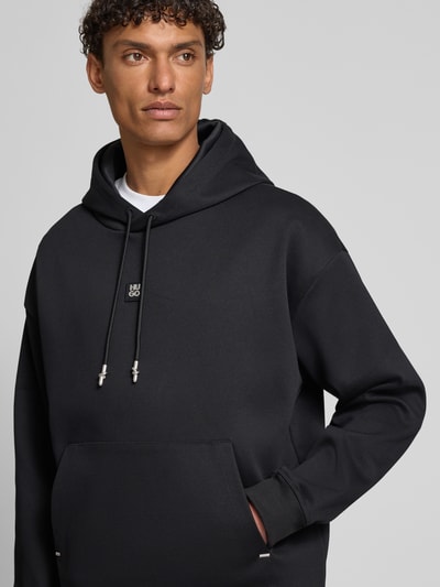 Männermodel trägt Regular Fit Hoodie aus Baumwoll-Mix Modell 'DINEO' von HUGO, Optik: Unifarben, Label-Stitching-Applikation, Label-Patch, Metall-Akzente, Kängurutasche, Kapuze mit Tunnelzug, Langarm, Ärmelabschluss und Rumpfabschluss: Gerippt, Materialverarbeitung: Sweat, Nahaufnahme Oberkörper.