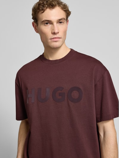 Männermodel trägt Oversized T-Shirt aus reiner Baumwolle Modell 'DINKEE' von HUGO, unifarben in Dunkelrot mit Label Print, Nahaufnahme Oberkörper.