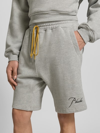 Männermodel trägt Sweatshorts aus Baumwoll-Mix von RHUDE, grau, Gerade Passform, elastischer Bund mit Tunnelzug, Label-Stitching, Eingrifftaschen, Nahaufnahme Oberschenkelbereich.