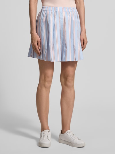 Frauenmodel trägt Ausgestellter Faltenrock aus reiner Baumwolle von Lacoste mit gestreiftem Allover-Muster in Blau, Rosa und Weiß, Popeline-Struktur mit elastischem Bund, Ganzkörperansicht von vorne.