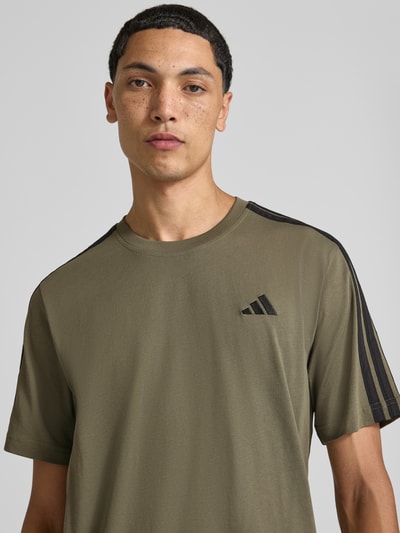Männermodel trägt Regular Fit T-Shirt aus reiner Baumwolle Modell 'M 3S SJ LC T' von adidas Sportswear in Khaki mit schwarzen Details, Nahaufnahme Oberkörper.