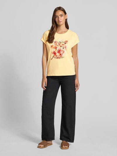 Frauenmodel trägt Damen T-Shirt mit Motiv-Print Modell 'RINA' von Soyaconcept in Gelb, Baumwoll-Elasthan-Mix, Regular-Fit, Rundhalsausschnitt, Ärmel mit Aufschlag, schwarze Hose, Ganzkörperansicht von vorne.
