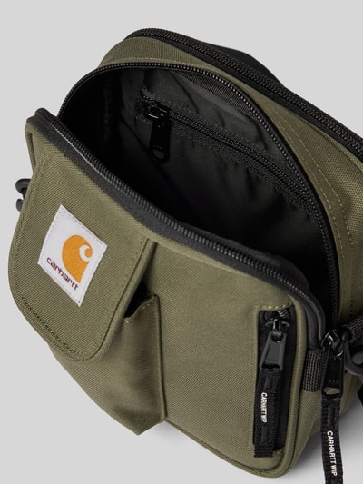 Produktfoto, Essentials Bag mit Logo-Patch von Carhartt Work In Progress in Olivgrün, Hauptfach mit Reißverschluss, abnehmbarer Schulterriemen, Reißverschlussfach innen, Maße 18x18x8 cm, Länge Schulterriemen 78 cm.