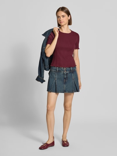 Frauenmodel trägt Slim Fit T-Shirt aus Baumwoll-Mix Modell 'TENNA' von ONLY in Bordeaux zu Jeansrock, Ganzkörperansicht von vorne, Damen T-Shirt von ONLY