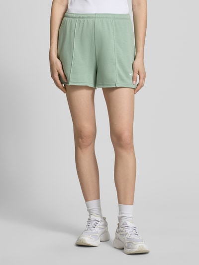 Frauenmodel trägt Regular Fit Shorts mit Tunnelzug von Nike in Mintgrün, Baumwoll-Mix, abgerundete Passform, Logo-Stitching, Ganzkörperansicht von vorne.