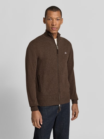 Męski model nosi Regular Fit Pullover aus reiner Wolle od GANT, jednokolorowy brązowy kardigan rozpinany z wyhaftowanym logo, okrągły dekolt, długi rękaw, prążkowane wykończenia, dzianina z czystej wełny, całkowity widok z przodu.