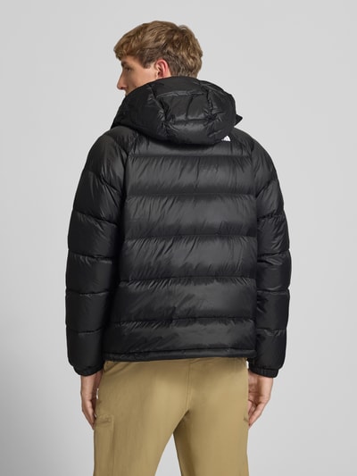 Mężczyzna model nosi kurtkę 'Jacke mit Logo-Stitching und Kapuze' od The North Face, czarna, prosty krój, kaptur, zamek błyskawiczny, boczne kieszenie zapinane na zamek błyskawiczny, wyhaftowane logo, długość tyłu w rozmiarze M: 66 cm, szerokość ramion: 45 cm, szerokość klatki piersiowej: 55 cm, długość rękawów: 70 cm, tekstura gładka, widok całej sylwetki z tyłu.