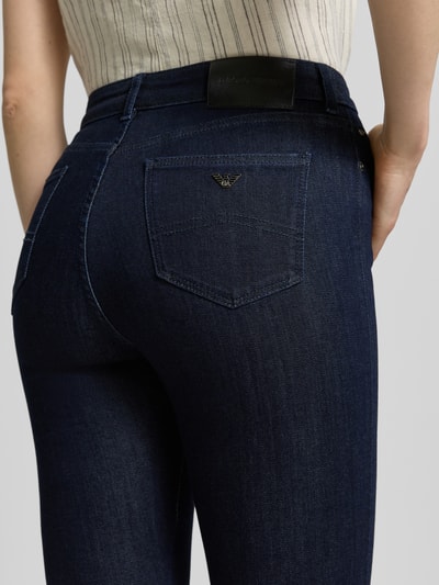 Frauenmodel trägt Slim Fit Jeans aus Viskose-Mix im 5-Pocket-Design von Emporio Armani, dunkelblau, glatte Textur, Nahaufnahme Rückansicht. Elastischer Viskose-Mix mit Lyocell-Anteil, Bundweite 35 cm, Innenbeinlänge 80 cm, Knopf- und Reißverschluss.
