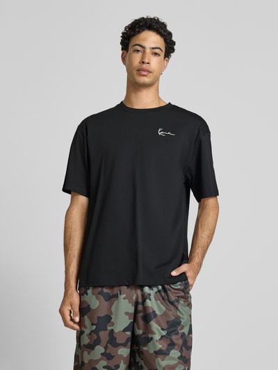 Männermodel trägt Oversized T-Shirt mit Logo-Stitching von KARL KANI aus reiner Baumwolle in Schwarz, Ganzkörperansicht von vorne.