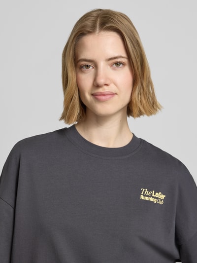 Männermodel trägt Oversized T-Shirt mit Label-Detail Modell 'Regina' von LeGer by Lena Gercke, czarna bawełna, dekolt okrągły, detailowe logo, długość tyłu 64 cm w rozmiarze 36, widok z przodu, półzbliżenie górnej części ciała.