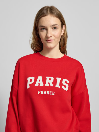 Frauenmodel trägt Oversized Sweatshirt aus Baumwoll-Mix Modell 'SWEAT LIFE' von Only in Rot mit weißem Motiv-Print, unifarben, Crew Neck, langarm, Nahaufnahme Oberkörper.