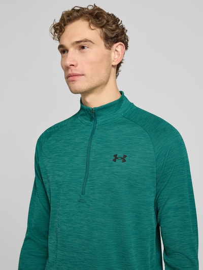 Mannenmodel draagt Sweatshirt mit kurzem Reißverschluss und Logo-Print van Under Armour in groen met logoprint, recht model, opstaande kraag, ruglengte maat M 74 cm, mouwlengte maat M 64 cm, detailopname bovenlichaam