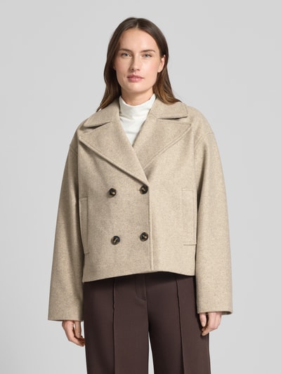 Frauenmodel trägt Cropped Trenchcoat mit doppelreihiger Knopfleiste Modell 'VINCELINE' von Vero Moda in Beige, Reverskragen, Boxy Fit, unifarbene Optik, seitliche Eingrifftaschen, melierte Textur, langarm, Ganzkörperansicht von vorne.