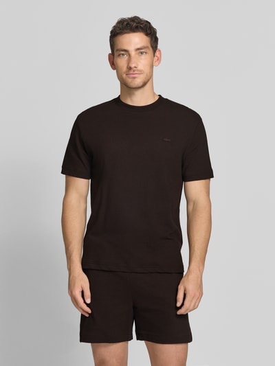 Męski model nosi Regular Fit T-Shirt aus reiner Baumwolle von Lacoste, czarny, krój regular fit, unicolor, label patch, okrągły dekolt, krótki rękaw, drobny dzianinowy materiał, widok całej sylwetki z przodu.