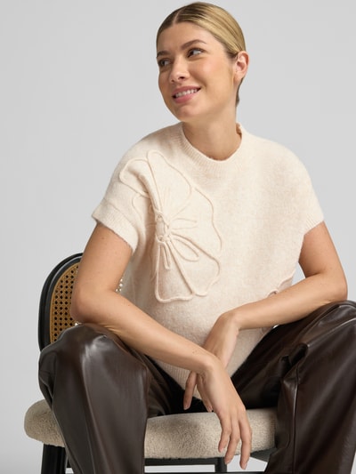 Vrouwenmodel draagt gebreid shirt met ronde hals Model 'OMEA' van b.young, elastische materiaalmix met wol, ribboorden, los model, ruglengte maat S 54 cm, mouwlengte 12 cm, lichtbeige tint, zachte textuur, decoratief bloemdetail, Nahaufnahme Oberkörper