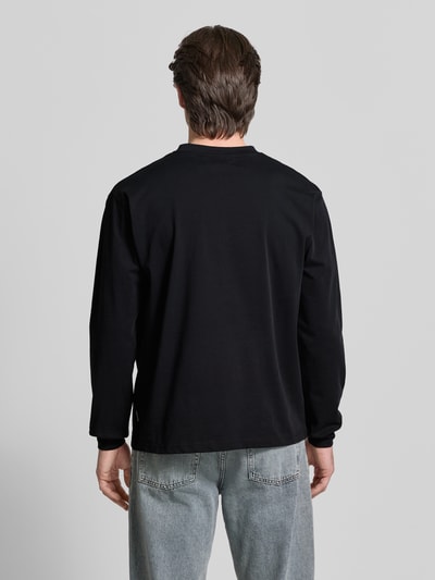 Męski model nosi Longsleeve mit Label-Stitching Modell 'Baine' od WOODBIRD, czarna bio-bawełna, krój regular fit, z okrągłym dekoltem, widok całej sylwetki z tyłu.