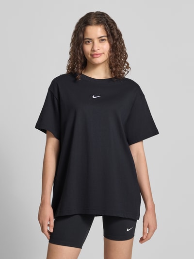 Kobiece modelka nosi Damski t-shirt z Logo i Okrągły dekolt od Nike z bawełny, krój oversized, czarny, Długość tyłu 68 cm, Ganzkörperansicht von vorne.