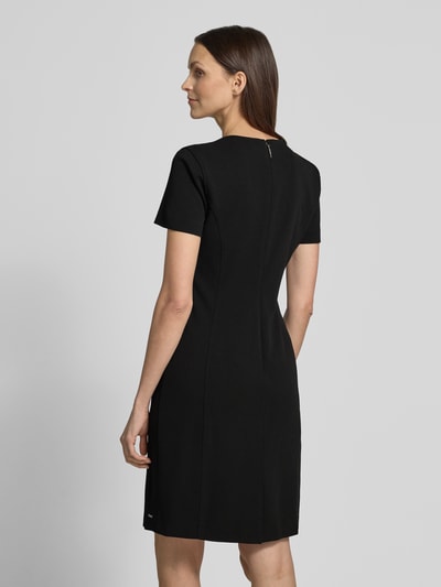 Modelka nosi 'Knielanges Etuikleid mit Rundhalsausschnitt' od Calvin Klein Womenswear, czarny materiał z dodatkiem stretchu, prosty krój, długość do kolan, okrągły dekolt, szerokość w rozmiarze S: 43 cm, długość z tyłu w rozmiarze S: 92 cm, długość rękawa w rozmiarze S: 19 cm, widok całej sylwetki z tyłu.