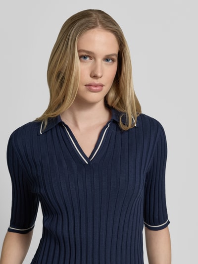 Frauenmodel trägt Slim Fit Poloshirt aus Viskose-Mix Modell 'SIMOSA' von Vero Moda, navy, Rippstrick, Kontraststreifen, Nahaufnahme Oberkörper.